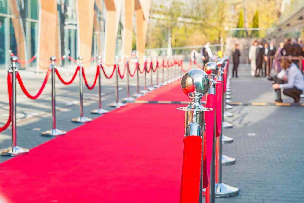 Close up red carpet ceremony with selective focus on the stanchions and the ropes with blurred guests and photographer background. Celebrity lifestyle concept.